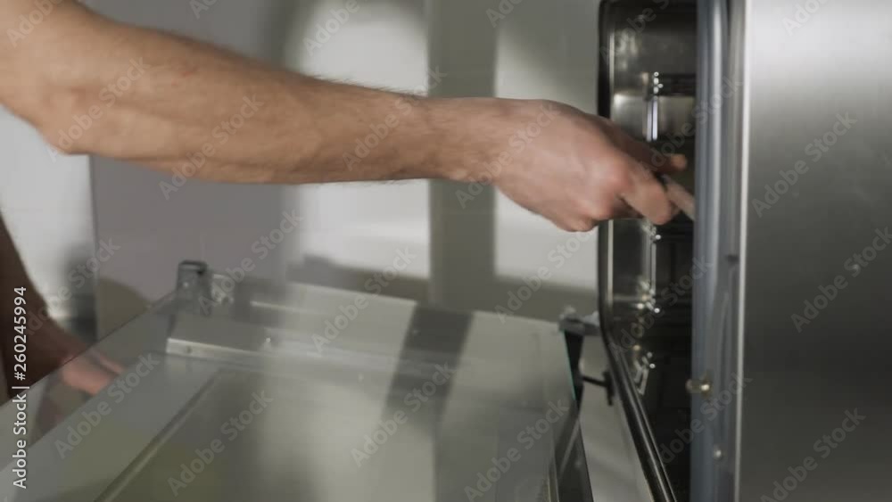 Baker puts on cinnamon rolls on a baking sheet in the oven to bake. Side view, hands close-up.