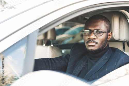 A young businessman in a suit sits at the wheel of a expensive car.