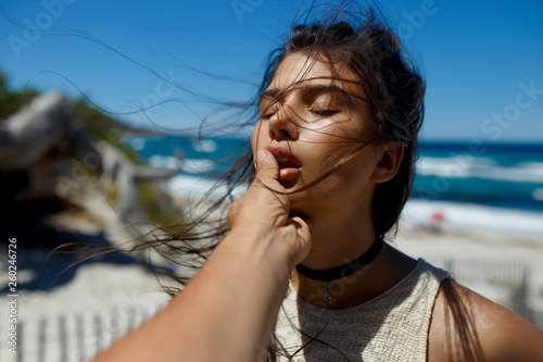 A loved one touches his girlfriend's lips, passion, love affair on the beach of the Corsica island, France, seascape background. Horizontal view.