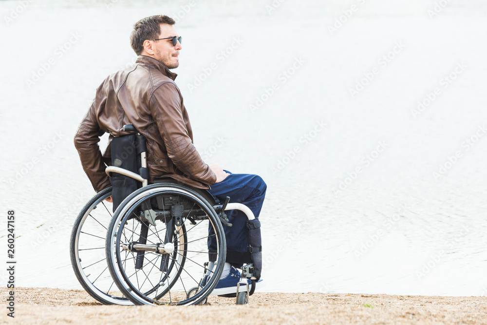 Young man sitting in a wheelchair by the lake.