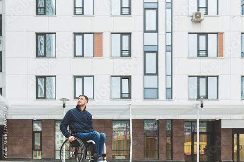 Young man in a wheelchair against the backdrop of a modern high-rise building.