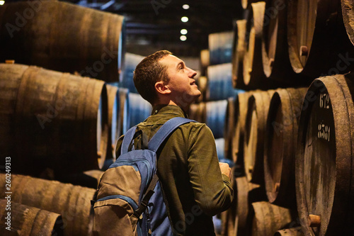 Young man tourist  walk in old aged traditional wooden barrels with wine in a vault lined up in cool and dark cellar in Italy, Porto, Portugal, France
