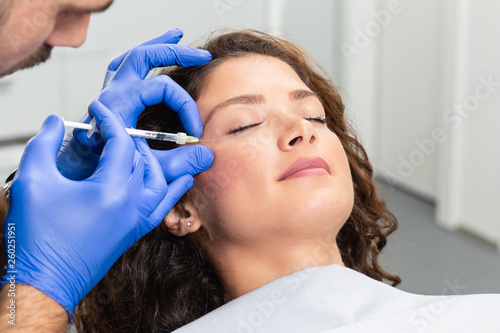 Attractive young woman is getting a rejuvenating facial injections. She is sitting calmly at clinic. The expert beautician is filling female wrinkles by hyaluronic acid.
