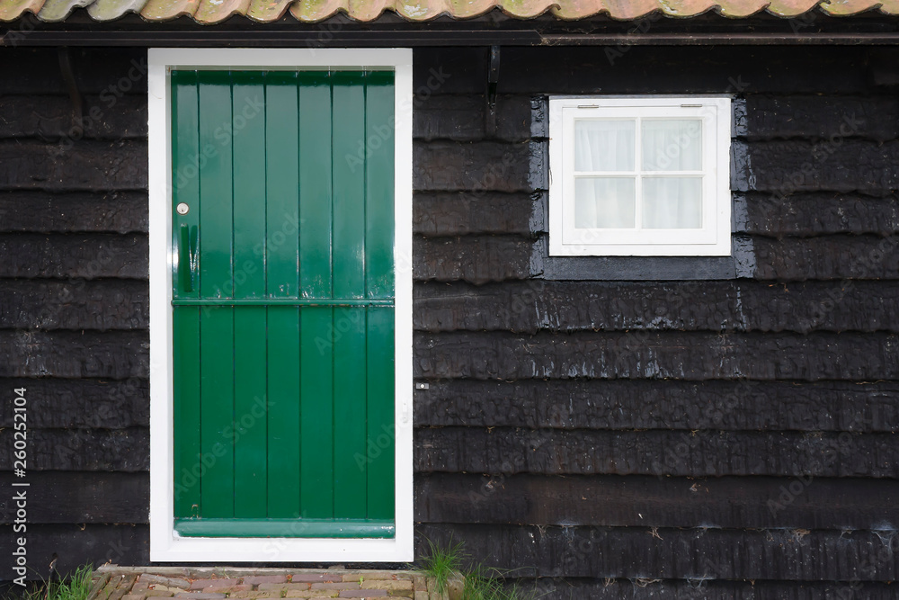 Front door of small rural cottage house with wooden wall and green door