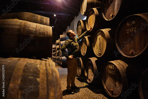 Professional winemaker male  in old aged traditional wooden barrels with wine in a vault lined up in cool and dark cellar in Italy, Porto, Portugal, France