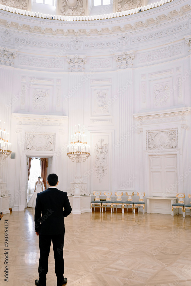 the groom meets the bride in a chic white lobby with high ceilings