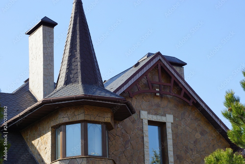 brown stone loft with windows and a tiled roof against a blue sky