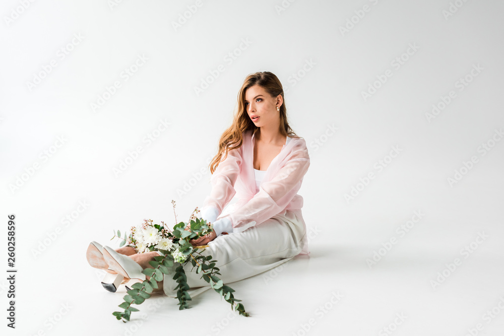 pretty young woman sitting with flowers and green eucalyptus on white
