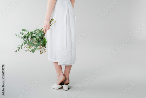 cropped view of girl in dress holding flowers while standing on grey