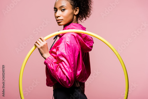 beautiful african american sportswoman holding hula hoop and looking at camera isolated on pink photo