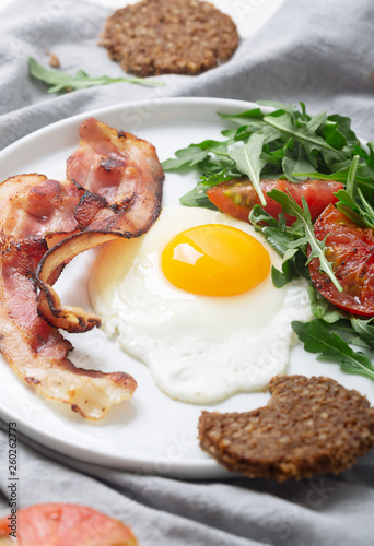 Hearty high protein english style breakfast with egg, fried bacon and arugula on the plate. Top view, vertical orientation