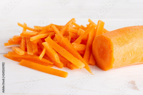 One half lot of pieces of fresh orange carrot cut into thin noodles on white wood