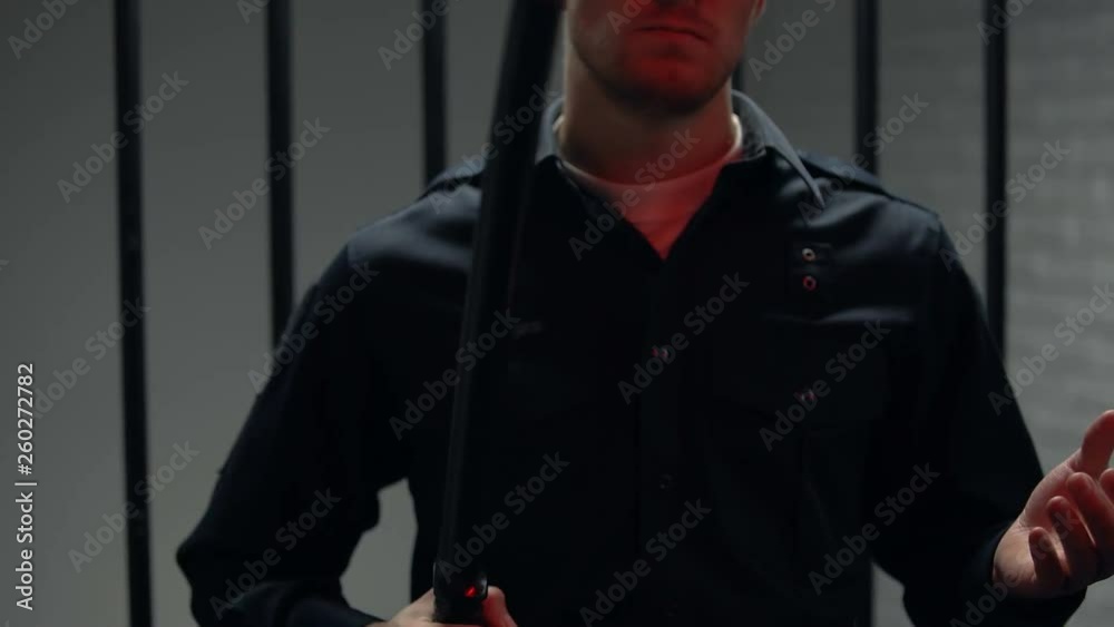 Warden standing near cell with truncheon, red lights blinking, revolt crackdown Warden standing near cell with truncheon, red lights blinking, revolt crackdown