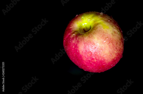 Water droplet on glossy surface of red apple on black background