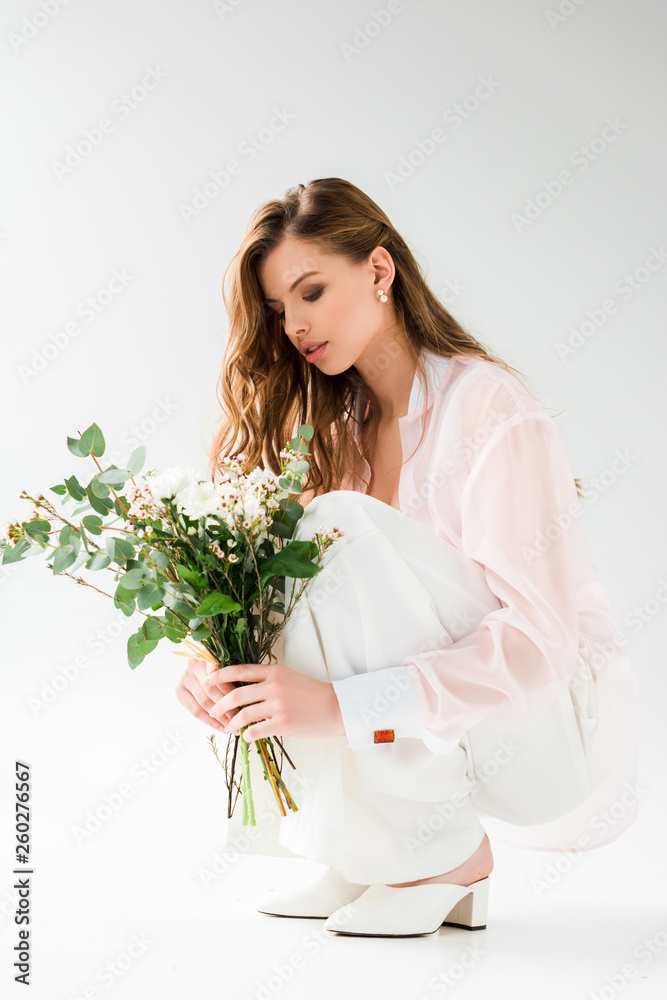 attractive woman looking at flowers with green eucalyptus leaves while sitting on white attractive woman looking at flowers with green eucalyptus leaves while sitting on white