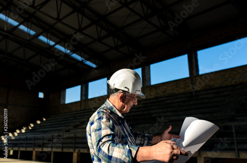 Senior construction manager with blueprint controlling building site.	