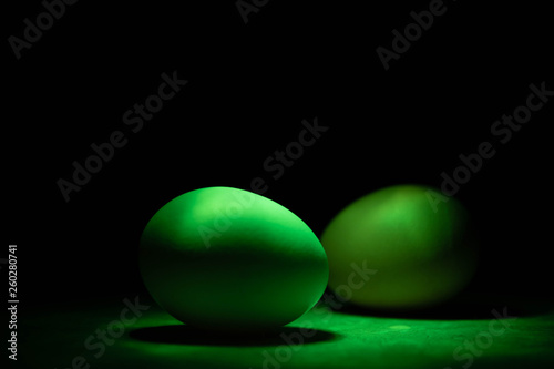 Unusual green chicken eggs in green light on black background
