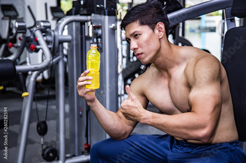 Asian fit man with energy drink relaxing and drinking in the gym. Sport and fittness concept.And Asian handsome muscles are tired, so drink Electrolyte drink.