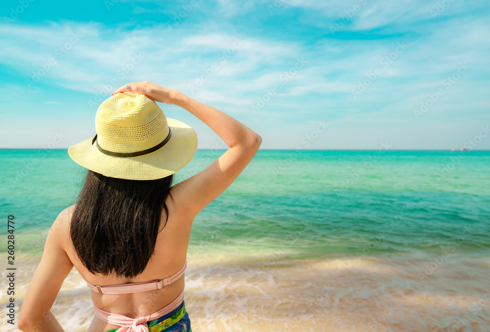 Back view of happy young Asian woman with straw hat relax and enjoy holiday at tropical paradise beach. Girl in summer vacation fashion. Beauty sexy model. Sand beach. Summer vibes. Summer travel.