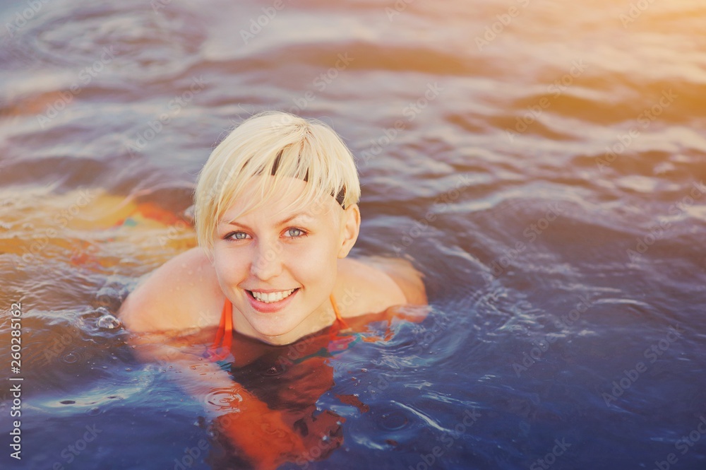 Geothermal spa. Happy smiling blonde woman relaxing and swimming in hot spring thermal pool. Girl enjoying bathing in a blue water lagoon Relaxing in a natural bath outdoor Wellness and health concept