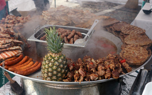 Traditional metal tray full of serbian street food. Among cevapcici, pljeskavica, various meat and boiled vegetables there is a big ananas. photo