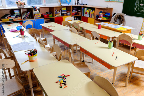 Room in elementary school, interior with light wooden furniture and learning aids on the walls. Pencils on the tables. No one, the children went for a walk