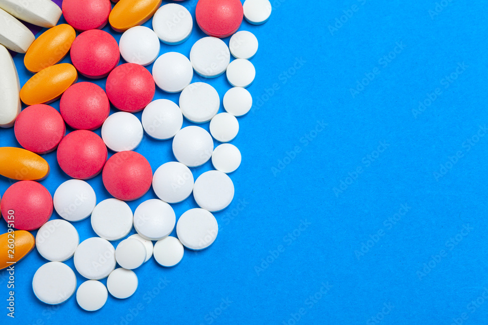 A pile of multicolored pills on blue background. Top view.