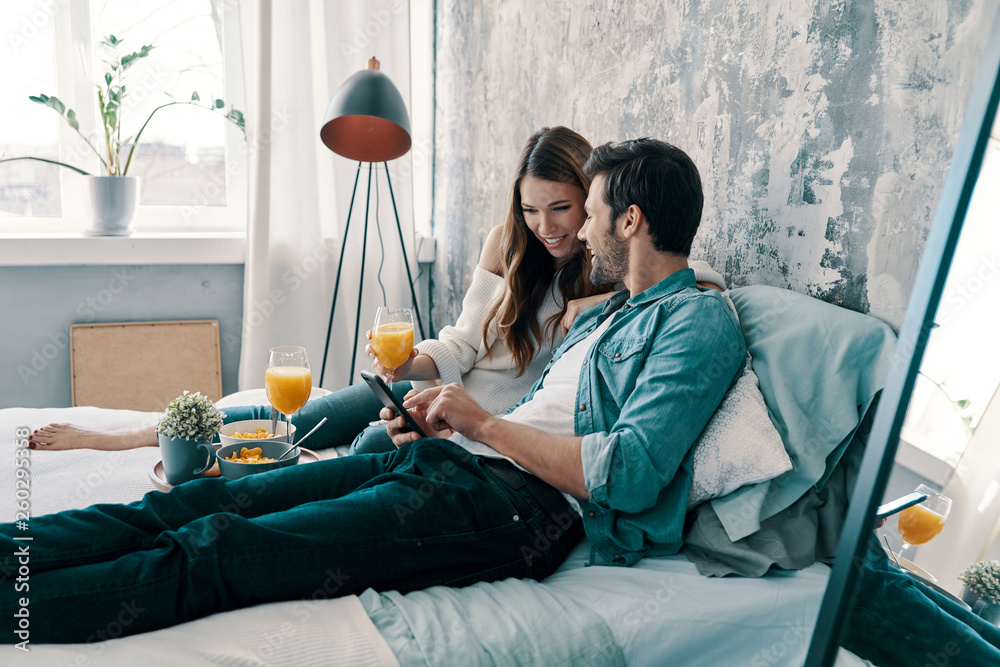 Obraz premium Searching for something online. Beautiful young couple having breakfast while spending time in bed at home