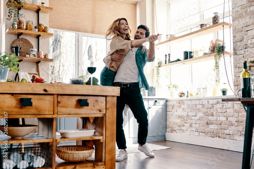 Playful. Full length of beautiful young couple in casual clothing dancing and smiling while standing in the kitchen at home photo