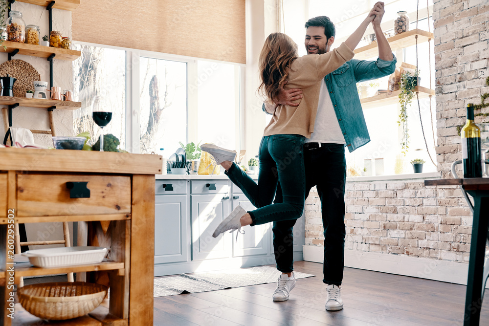 Romance. Full length of beautiful young couple in casual clothing dancing and smiling while standing in the kitchen at home - obrazy, fototapety, plakaty 