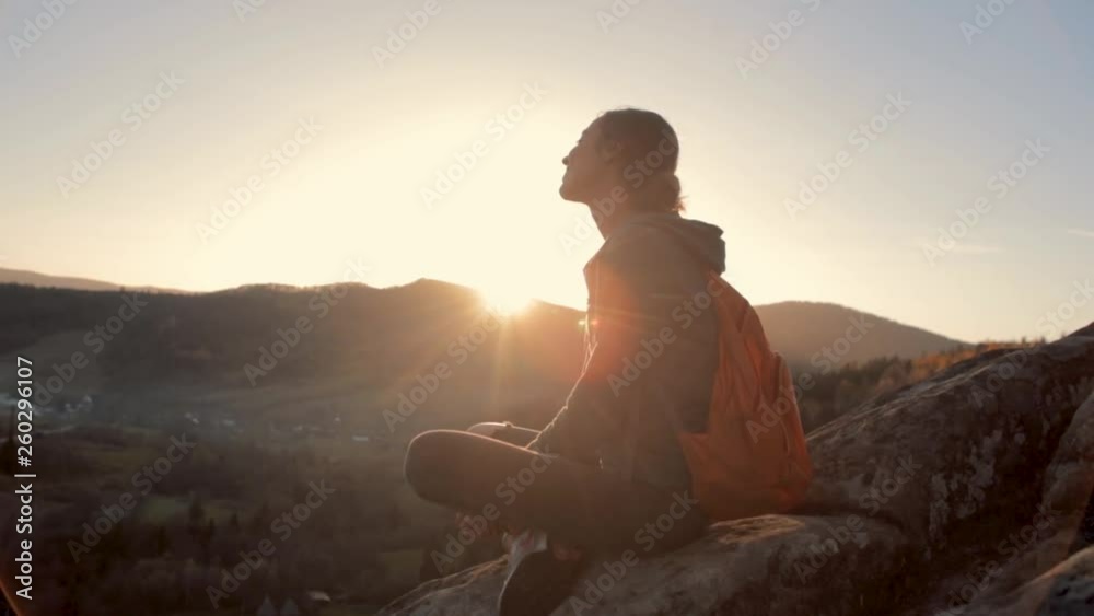 woman hiker with backpack sits on edge of cliff against background of sunrise woman hiker with backpack sits on edge of cliff against background of sunrise