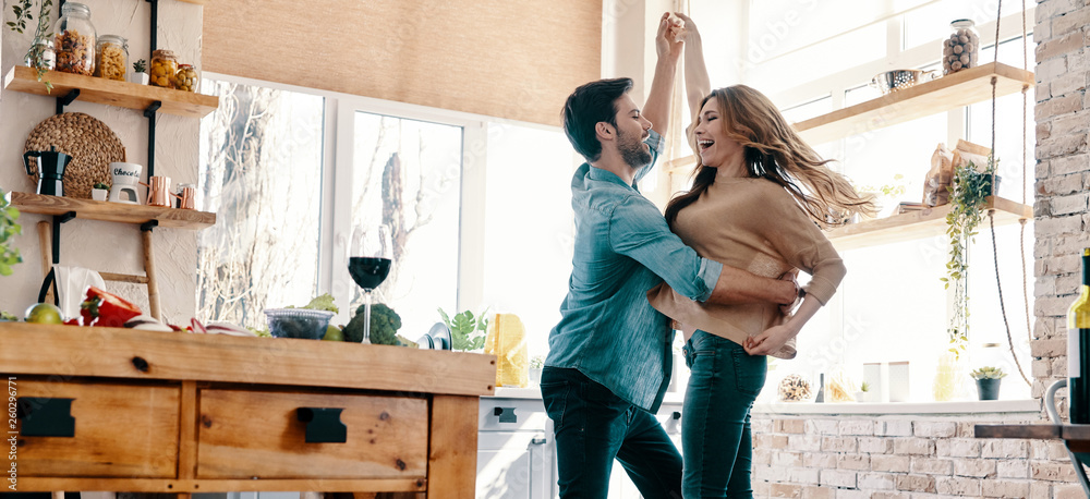 Simple joy of loving. Full length of beautiful young couple in casual clothing dancing and smiling while standing in the kitchen at home - obrazy, fototapety, plakaty 