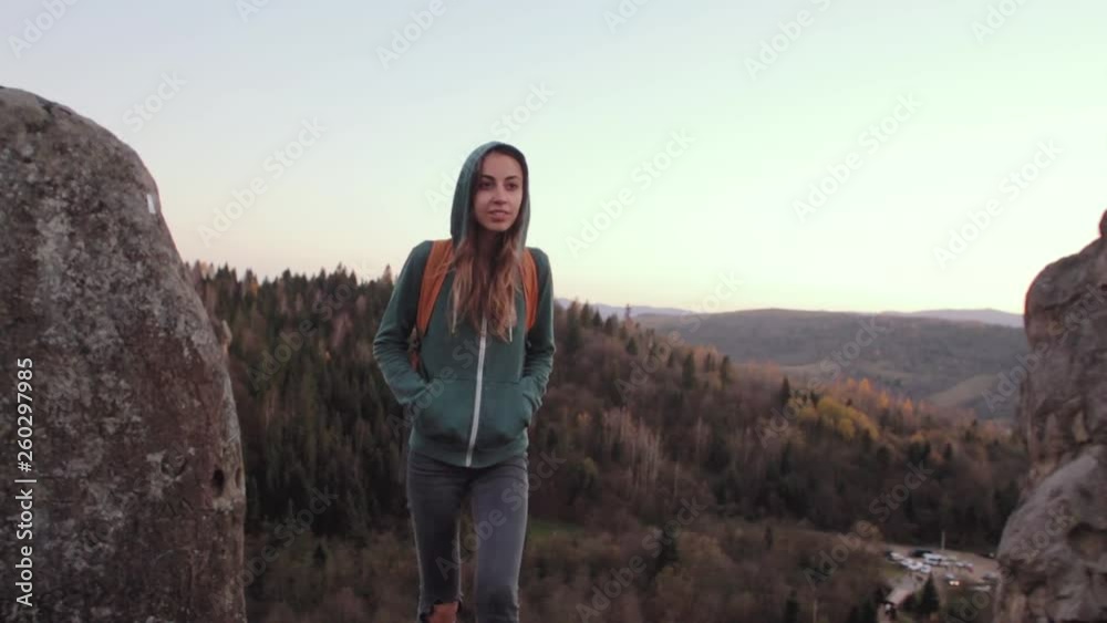 smiling woman hiker with backpack standing and walking on edge of cliff against a forest background smiling woman hiker with backpack standing and walking on edge of cliff against a forest background