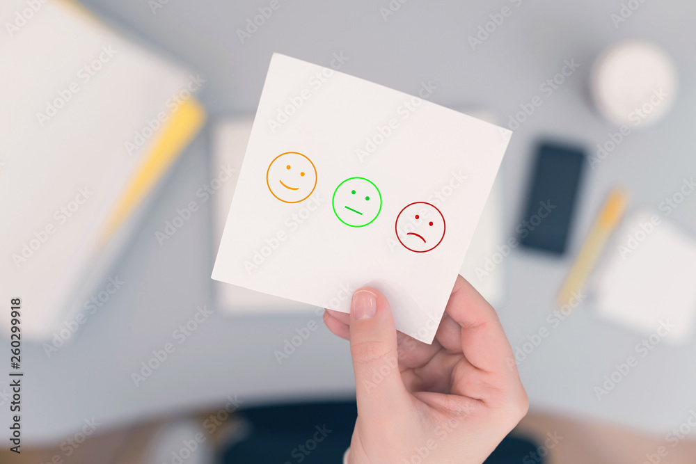 Woman clerk in the office holding paper sticker with set faces scale feedback. Customer satisfaction symbol. Woman clerk in the office holding paper sticker with set faces scale feedback. Customer satisfaction symbol.