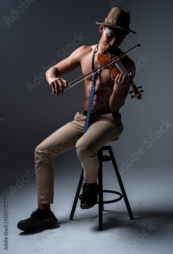 Thw handsome man show body muscle ,sitting on black chair,playing violin with happy feeling,vintage and art tone