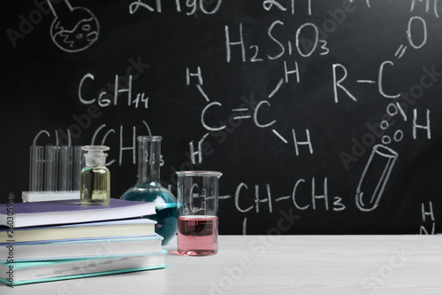 Laboratory glassware and school supplies on table against blackboard with chemical formulas