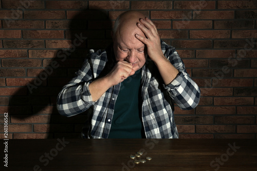 Poor senior man with coins at table near brick wall
