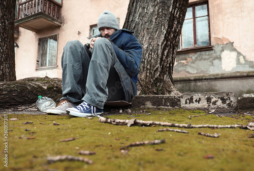Poor homeless man sitting on ground outdoors
