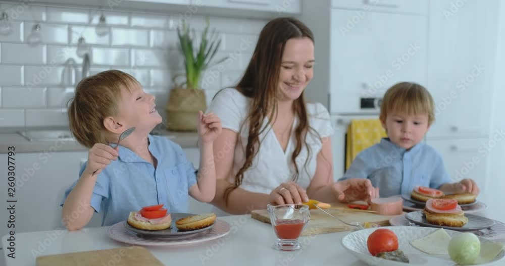 Mom with two children in the kitchen at the table preparing burger for lunch Mom with two children in the kitchen at the table preparing burger for lunch