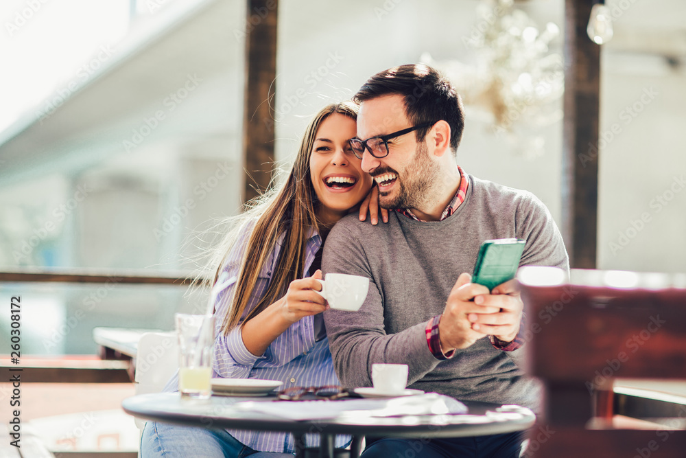 Young cheerful man and woman dating and spending time together in cafe, using phone. Young cheerful man and woman dating and spending time together in cafe, using phone.