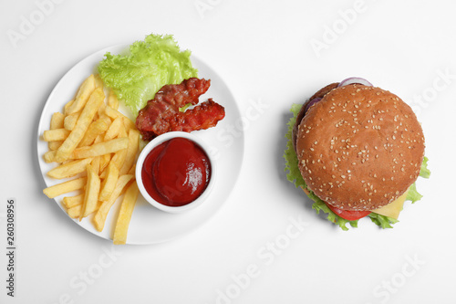Fresh burger and plate with french fries on white background, top view