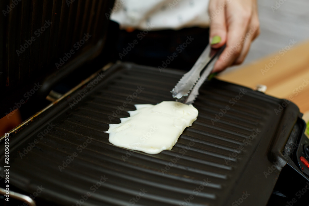 Girl fries a piece of cheese on the grill