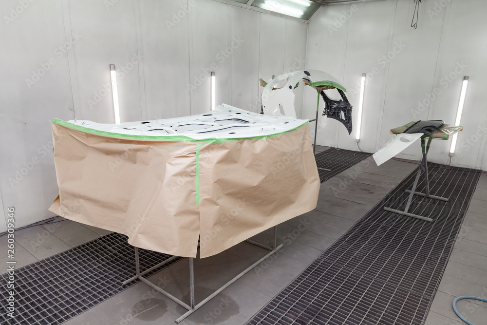 Painting and drying in a professional box of car body parts after applying putty and paint on inner side hood in the body repair shop with white lanterns in the working environment. Painting and drying in a professional box of car body parts after applying putty and paint on inner side hood in the body repair shop with white lanterns in the working environment.