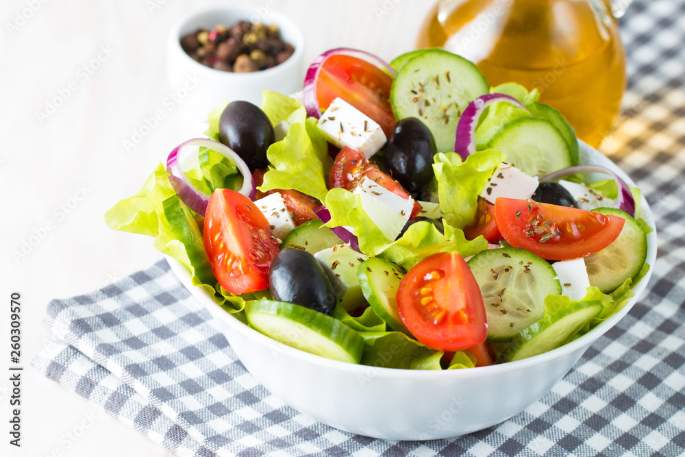 Fresh Greek salad made of cherry tomato, ruccola, arugula, feta, olives, cucumbers, onion and spices. Caesar salad in a white bowl on wooden background. Healthy organic diet food concept.