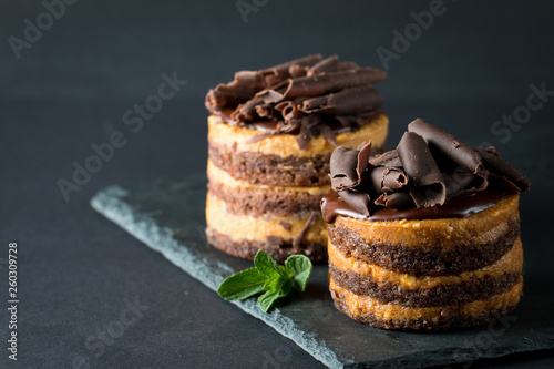 Chocolate cakes on black slatter board with mint, coffee beans on dark background, closeup photo. Fresh, tasty dessert food concept. 