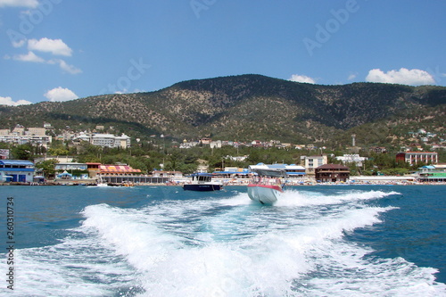 A panorama of the resort town from the board of a speed boat, which turns the blue sea surface into a white foam.