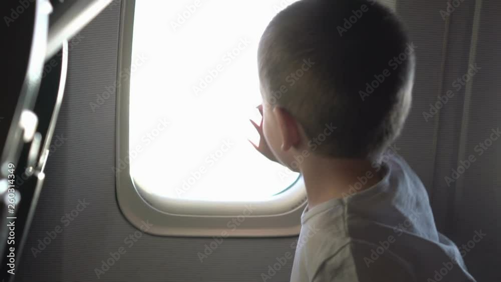 Young cute boy sitting on the seat and opens up airplane window