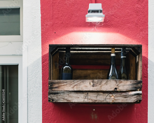 Wine Bottles in a wooden box on a red wall. 