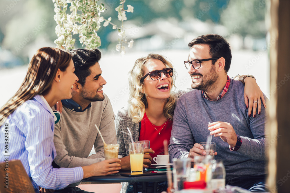 Fototapeta premium Group of four friends having fun a coffee together. Two women and two men at cafe talking laughing and enjoying their time