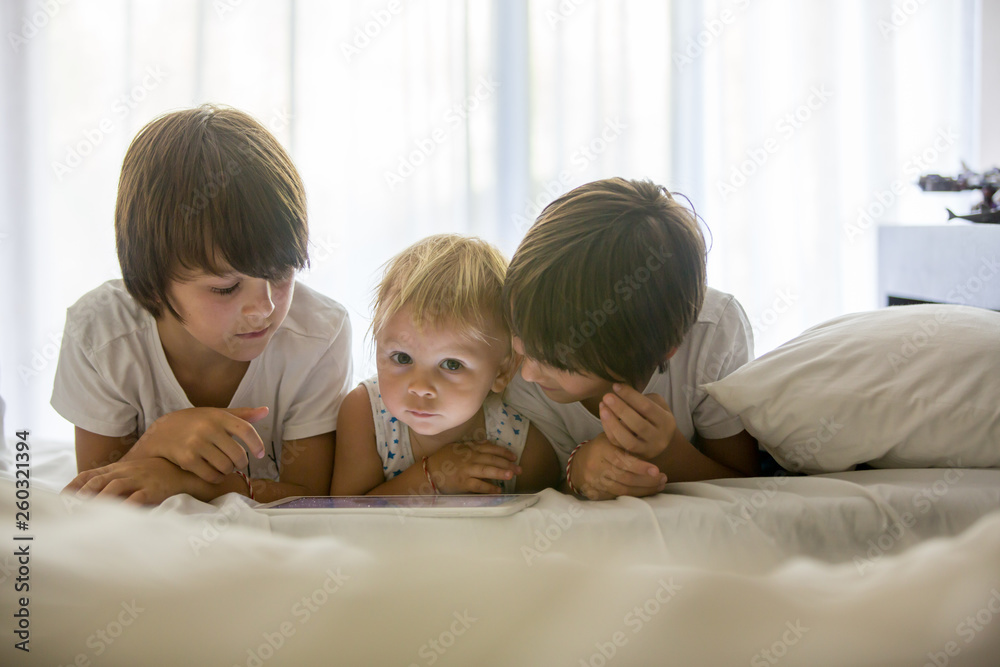 Brothers, playing in bed on tablet, enjoying summer holiday